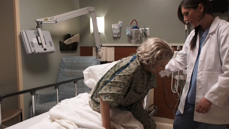 A doctor helping a patient stand up after a long period of lying in a hospital bed