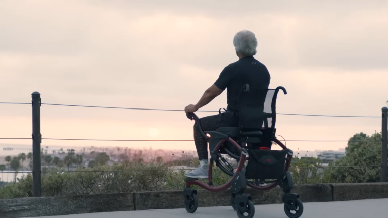 An Elderly Man Is Sitting in A Wheelchair, Looking out At a Peaceful Sunset Over a Landscape