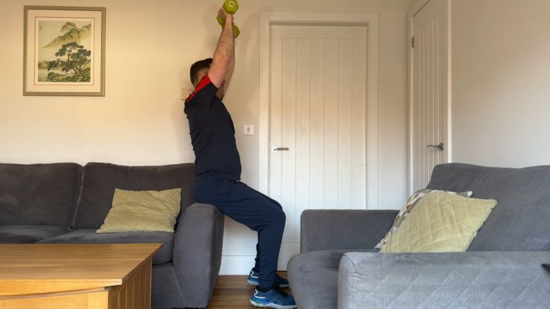 A Man Performing a Standing Overhead Press Exercise at Home, Demonstrating how Physical Activity and Mobility May Be Affected by Hernias