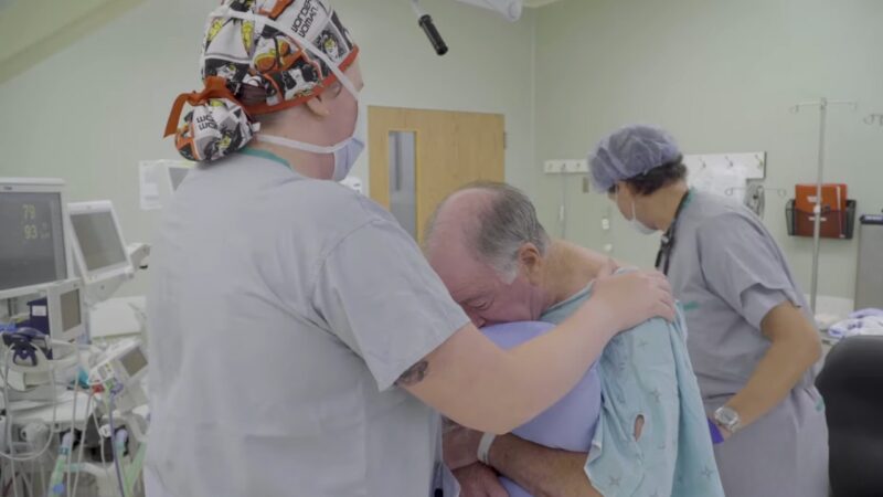 A Nurse Comforts an Elderly Patient in A Hospital Recovery Room While Another Medical Professional Assists Nearby