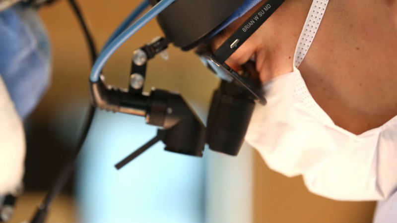 A Surgeon Wearing a Head-Mounted Device Inspects a Patient During a Procedure Related to Spondylolisthesis