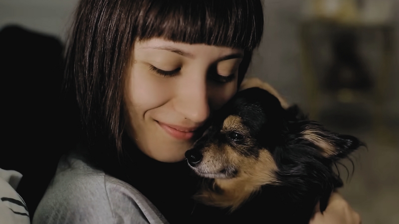 A Young Woman with A Gentle Smile Cuddles Closely with A Small Dog