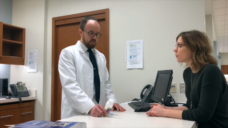 A Pharmacist in A White Coat Explains a Medication to A Patient Across the Counter