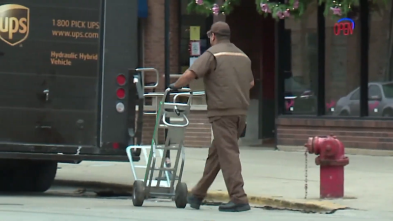 A Delivery Worker Unloading Packages with A Hand Truck Near a UPS Van