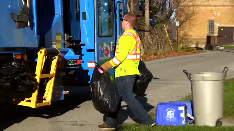 A Sanitation Worker Collecting Trash Bags Near a Garbage Truck on A Residential Street