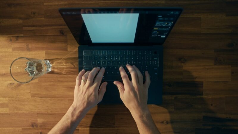 A top-down view of hands typing on a laptop keyboard, with a blank document open on the screen