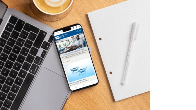 A smartphone displaying a National Institutes of Health webpage rests on a laptop keyboard
